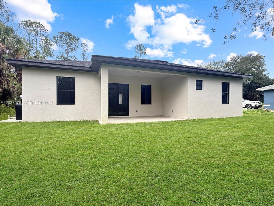 Rear exterior featuring a covered patio, smooth stucco finish, dark framed windows, and a dark shingle roof