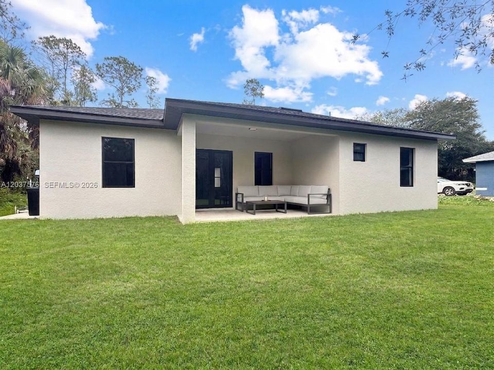 Virtual staged rear exterior featuring a covered patio, stucco finish, and dark-framed windows