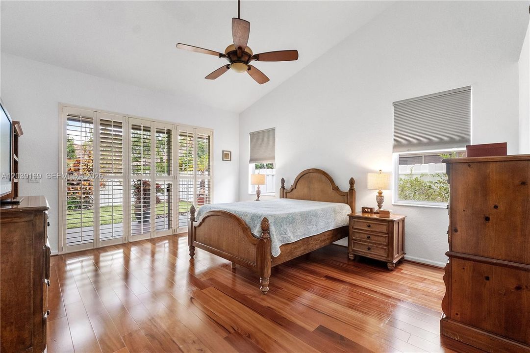 Large primary bedroom with engineered wood flooring & plantation shutters on doors to patio