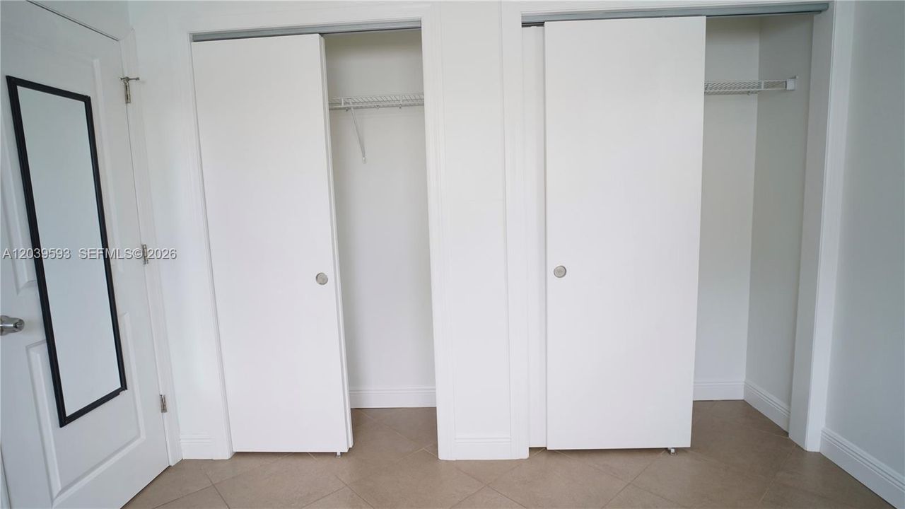 Dual closets featuring white sliding doors and integrated shelving, complemented by tile flooring