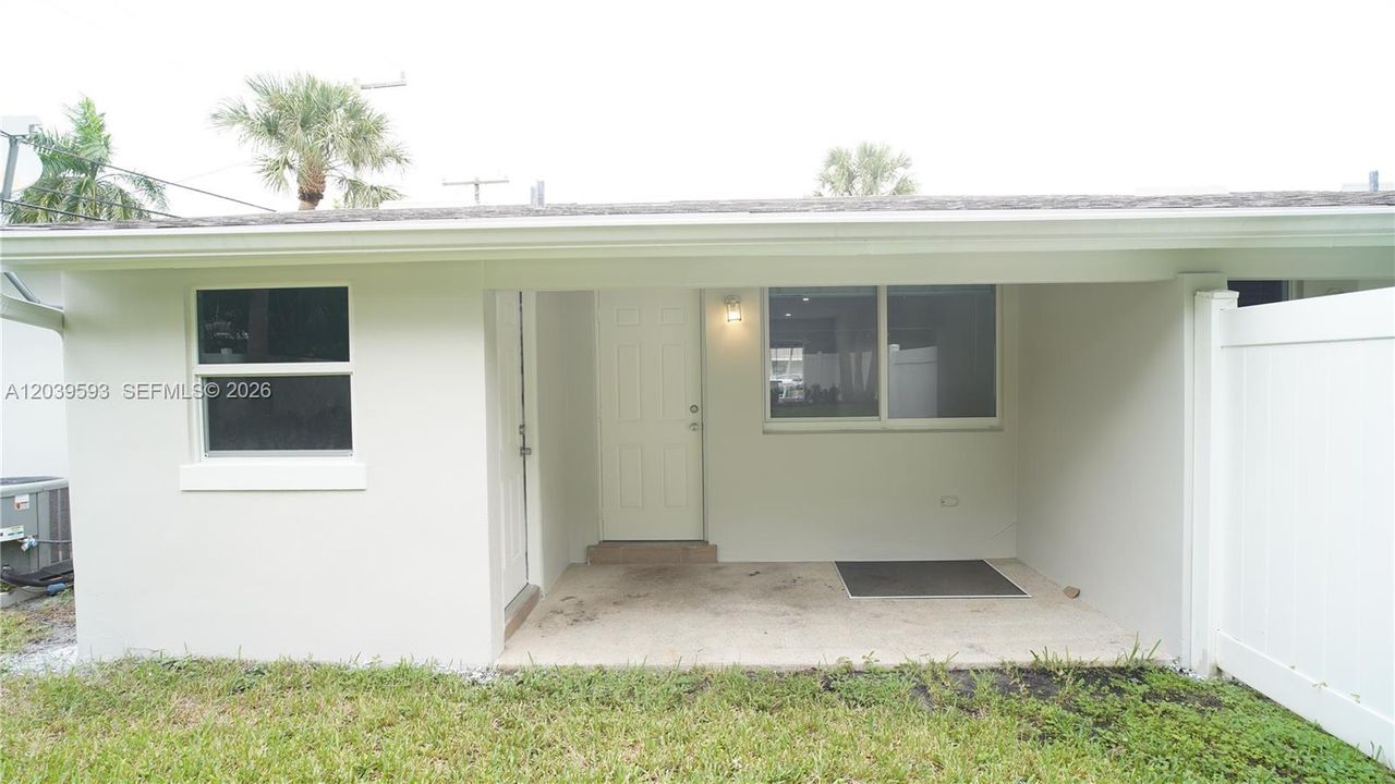 Exterior facade featuring a covered entryway, single-pane windows, and a white privacy fence