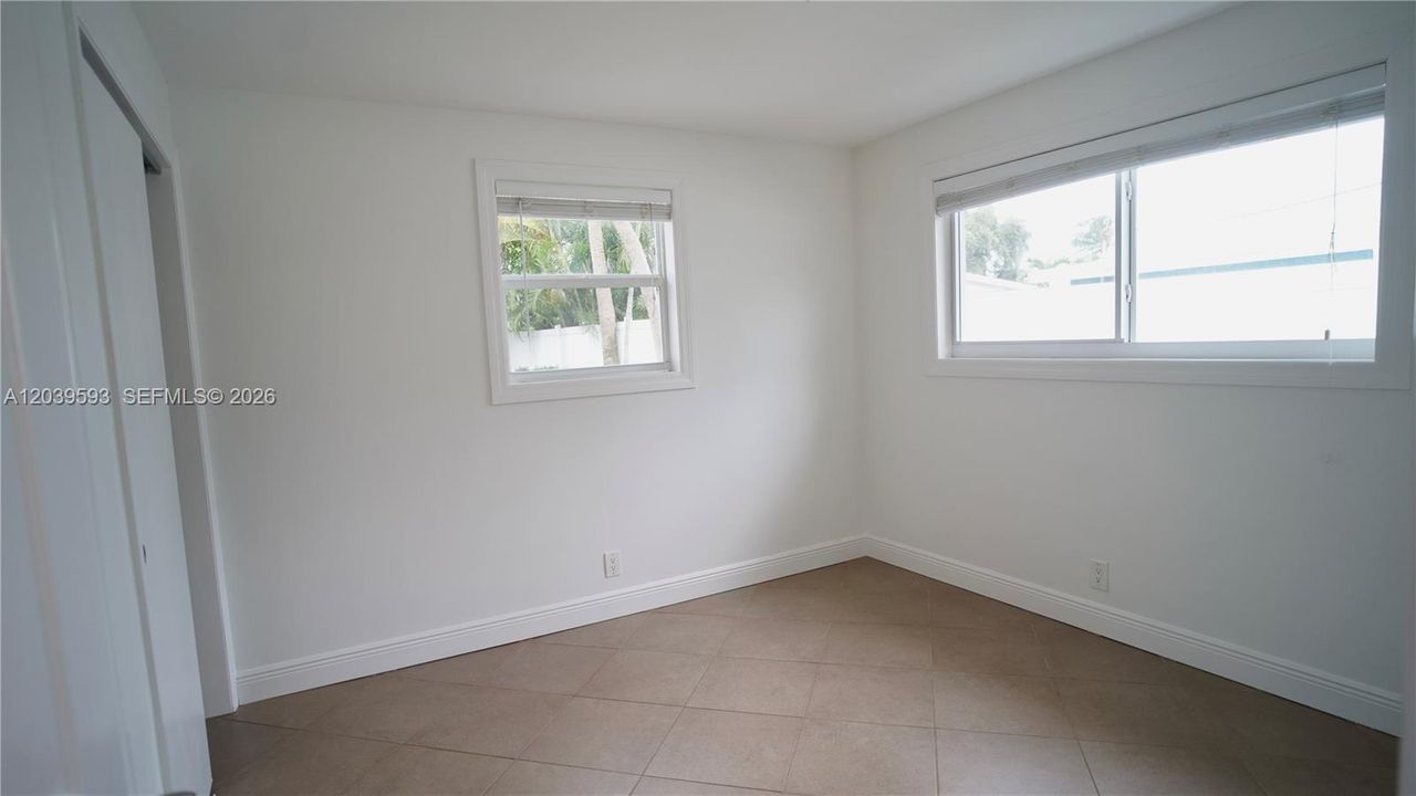 Neutral-toned interior space featuring large-format tile flooring, dual windows with installed blinds, and a built-in closet with sliding doors