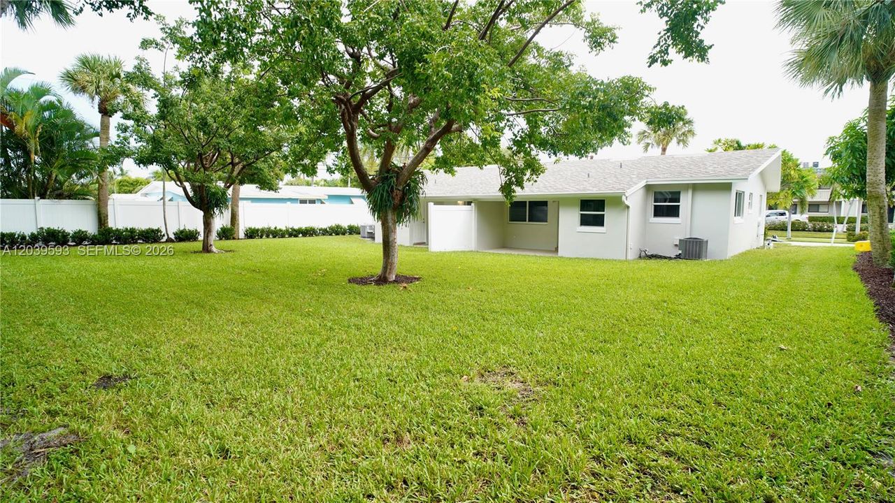 Expansive backyard featuring a sprawling lawn, mature shade trees, perimeter privacy fencing, and a covered concrete patio
