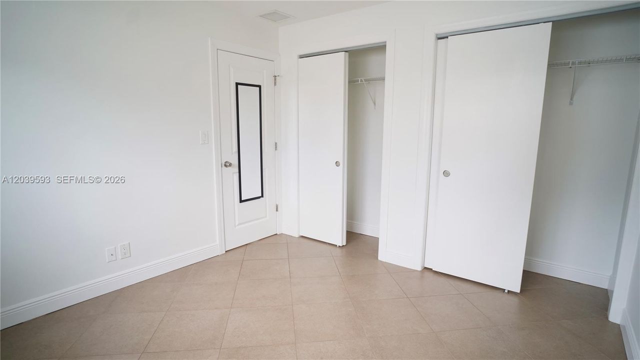 Neutral-toned tile flooring, two closets with white panel doors, and a single interior door featuring a built-in vertical mirror