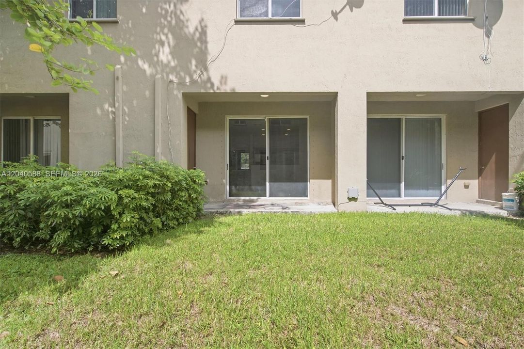Expansive green lawn with mature shrubbery, featuring two sets of sliding glass doors and a private patio space