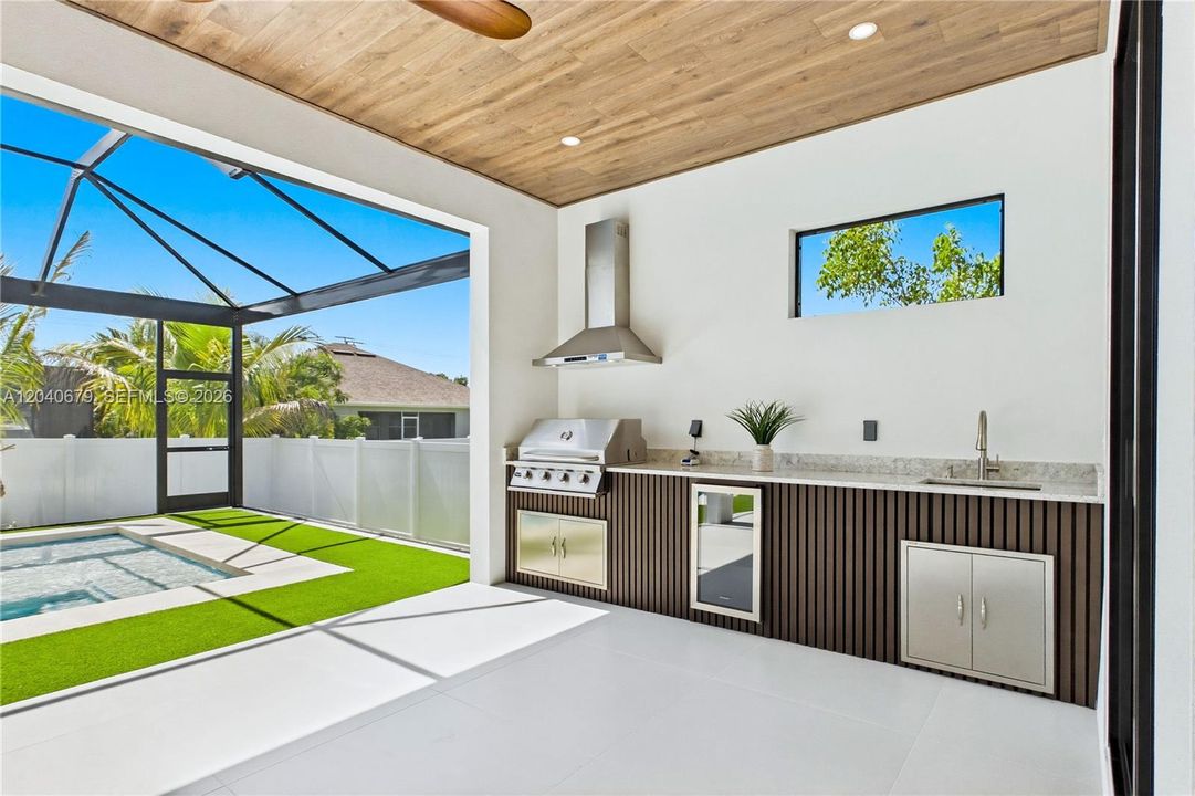 Outdoor kitchen is fully equipped w/ grill, hood vent, mini refrigerator & commercial-grade sink