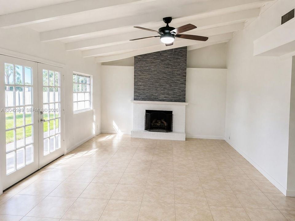 Bright and spacious living room featuring vaulted ceilings, tile flooring, a decorative fireplace, and French doors that provide abundant natural light and access to the backyard.
