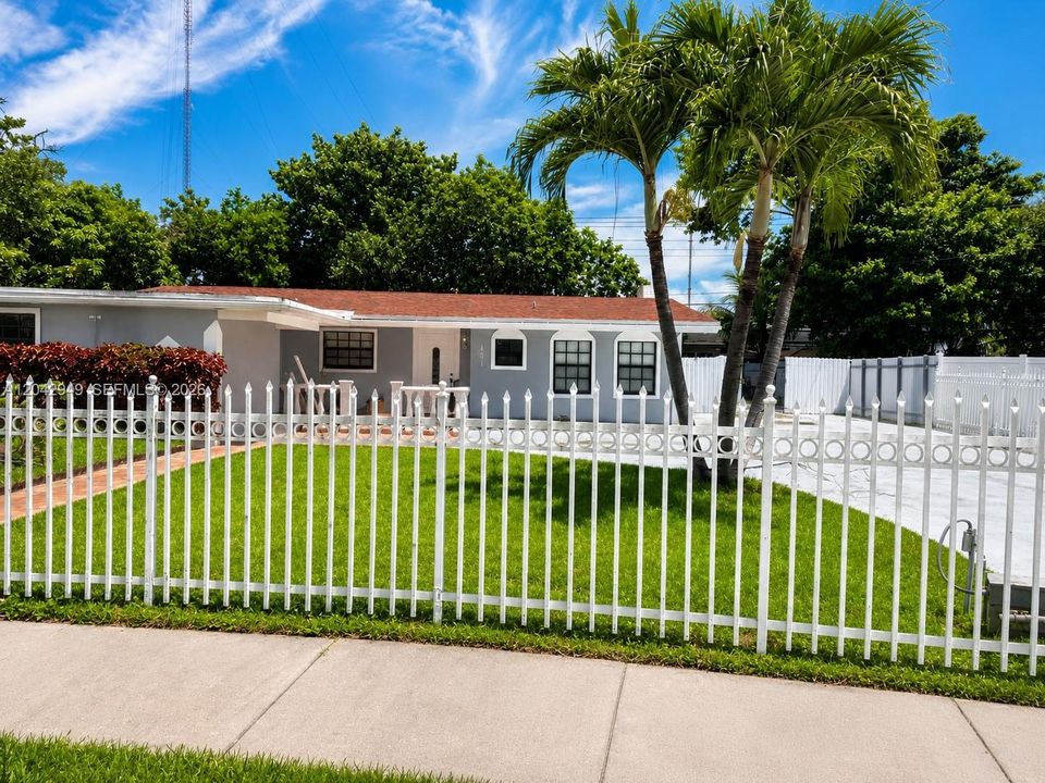 Front elevation featuring a fully fenced yard, mature palm trees, and ample parking.