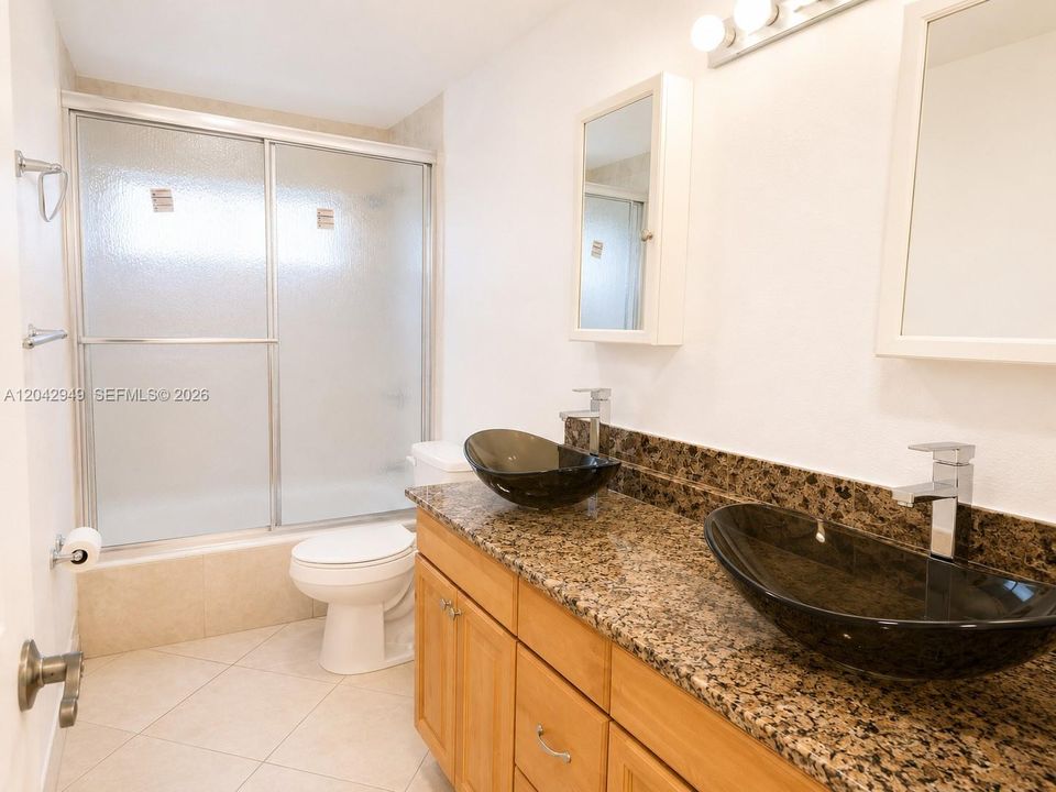 Bathroom with dual vessel sinks, granite countertops, and a spacious shower for everyday comfort.