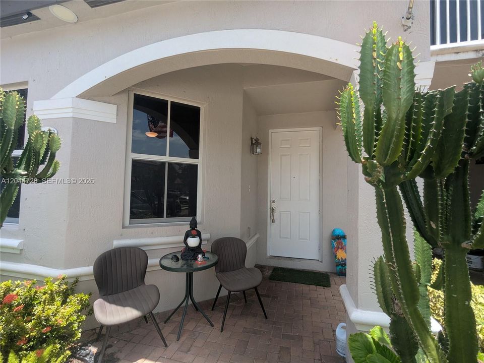 Cozy front porch with brick flooring, arched entry, and seating area. Clean and inviting space with decorative touches and private front access.