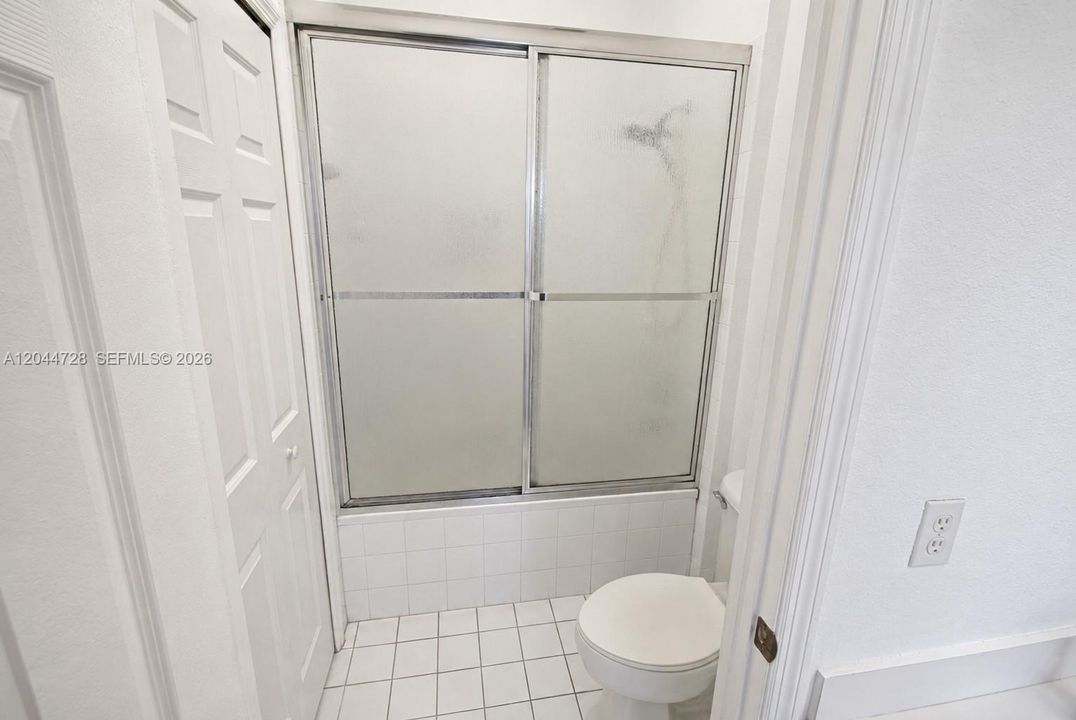 1st Master Bathroom with white tile flooring, tub with sliding glass doors, and a simple, functional layout