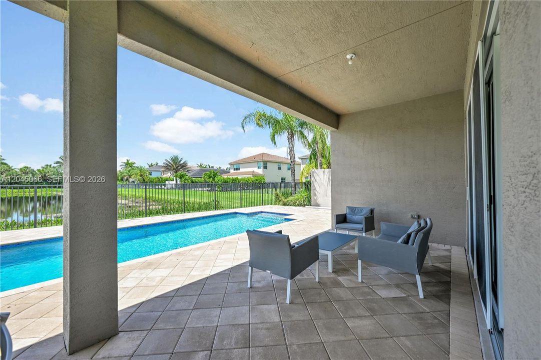 Covered concrete patio featuring tiled flooring, built-in recessed lighting, an in-ground swimming pool, and metal perimeter fencing
