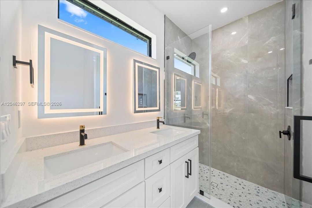 Spa-inspired bathroom featuring a dual-sink quartz vanity, illuminated designer mirrors