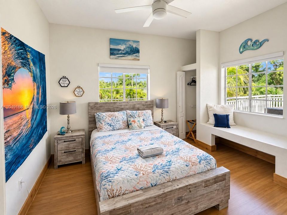 Room featuring wood-finish flooring, dual grid-pattern windows, a built-in window seat, and a ceiling fan
