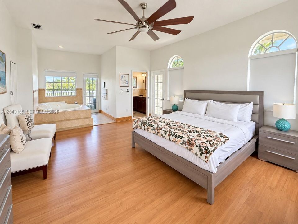 Spacious room featuring wood-finish flooring, vaulted ceilings with a multi-blade ceiling fan, arched windows, and a built-in jetted soaking tub with a tiled surround
