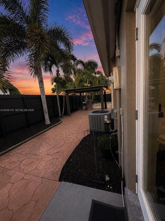 Side elevation showcasing the expansive insulated covered patio with integrated rain gutters, extensive concrete walkways, and hurricane shutters for added protection and peace of mind.