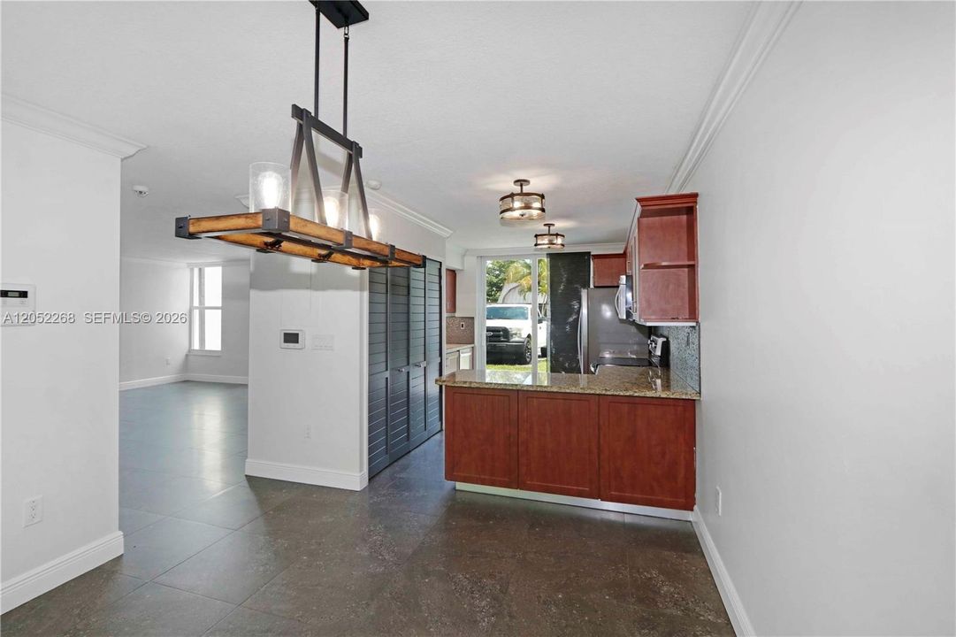 Moderna cocina de concepto abierto con elegantes gabinetes de madera, encimeras de granito y un distintivo candelabro estilo industrial, integrada a un luminoso espacio de estar con pisos de porcelanato