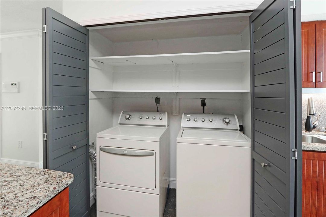Práctico cuarto de lavado integrado en la cocina, equipado con electrodomésticos eficientes y estanterías superiores para almacenamiento adicional, todo oculto tras elegantes puertas de lamas