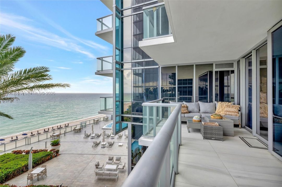 Balcony overlooking the resort-style pool and beachfront. Current furniture differs from what is shown.