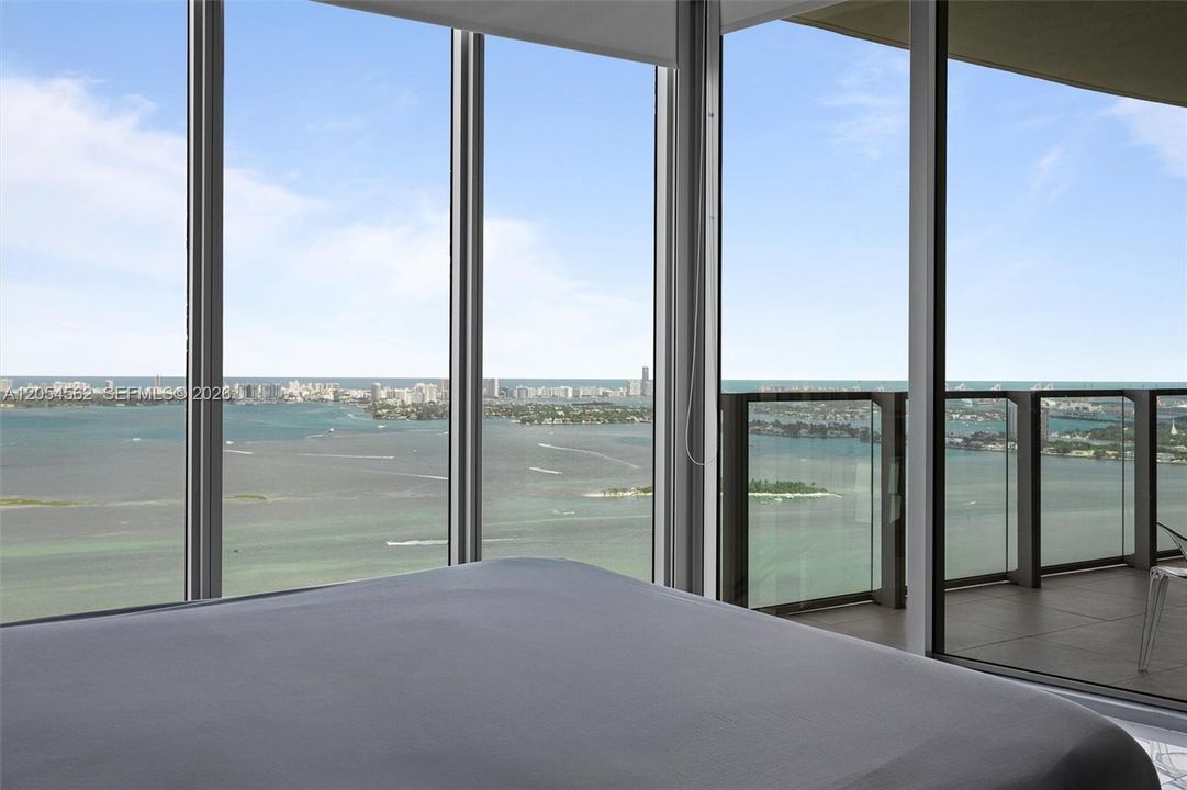 Primary suite wrapped in floor-to-ceiling windows with direct Biscayne Bay views