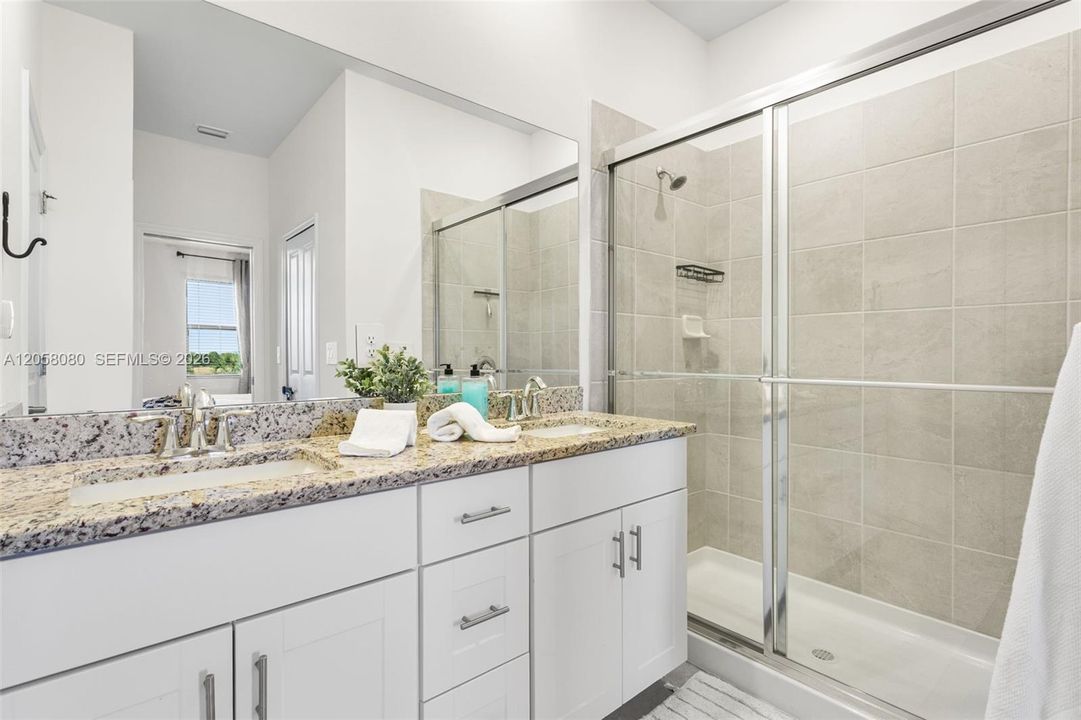 Spacious primary bathroom featuring a dual-sink granite vanity, glass-enclosed walk-in shower, and private water closet