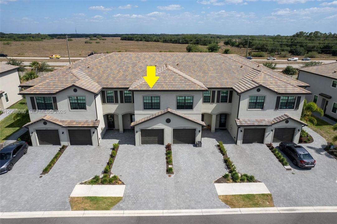 Aerial view highlighting the townhome’s attractive exterior, attached one-car garage, driveway parking for an additional vehicle, plus convenient guest parking nearby