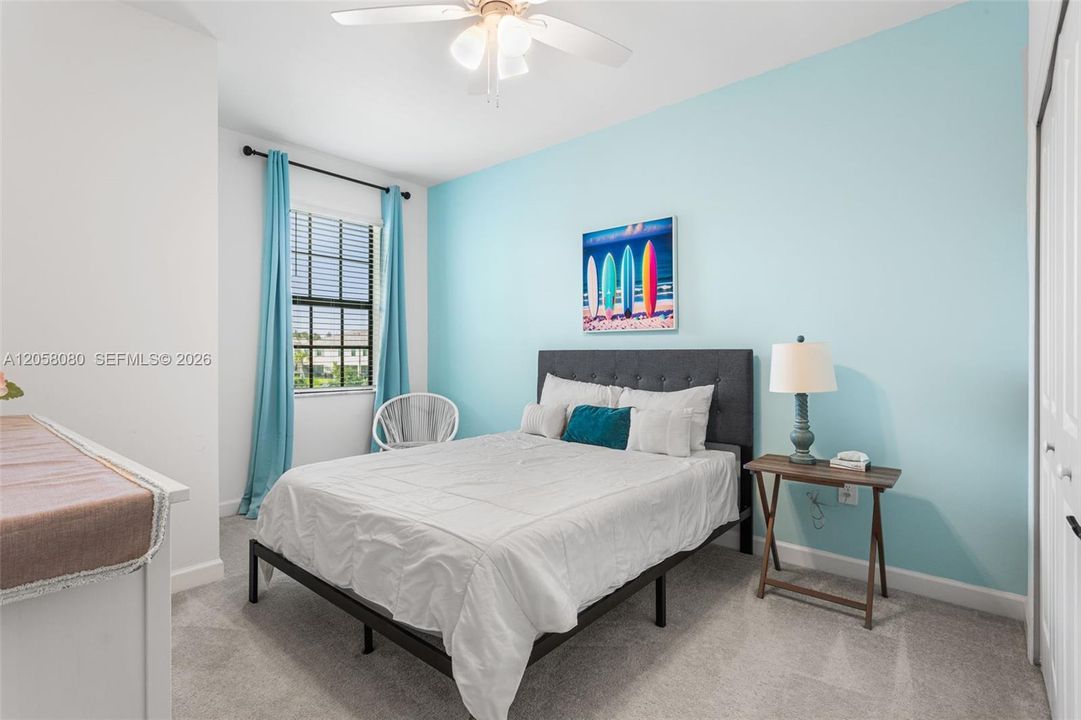 Bright third bedroom featuring a cheerful accent wall, ceiling fan, generous closet space, and plenty of natural light