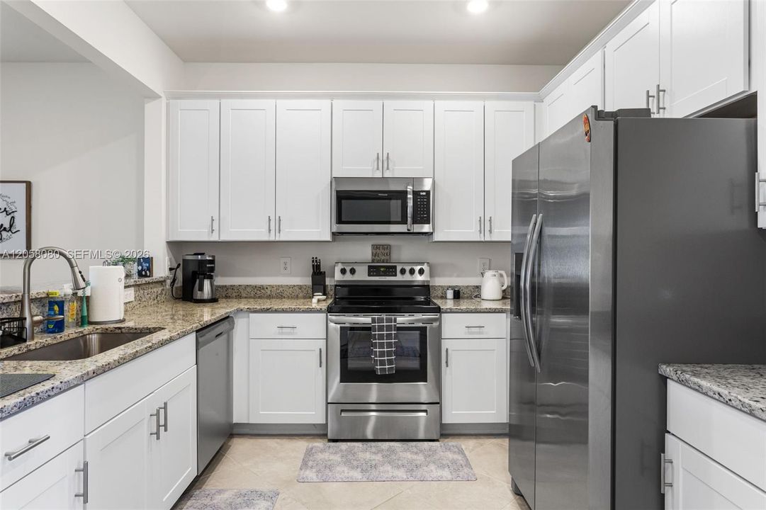 The spacious kitchen boasts granite countertops, stainless steel appliances, a deep sink, and white shaker cabinets