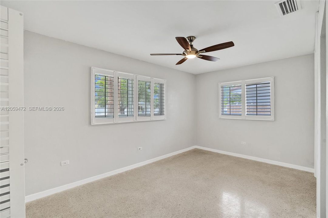 Spacious bedroom featuring light colors, terrazzo flooring, and ceiling fan for year-round comfort.