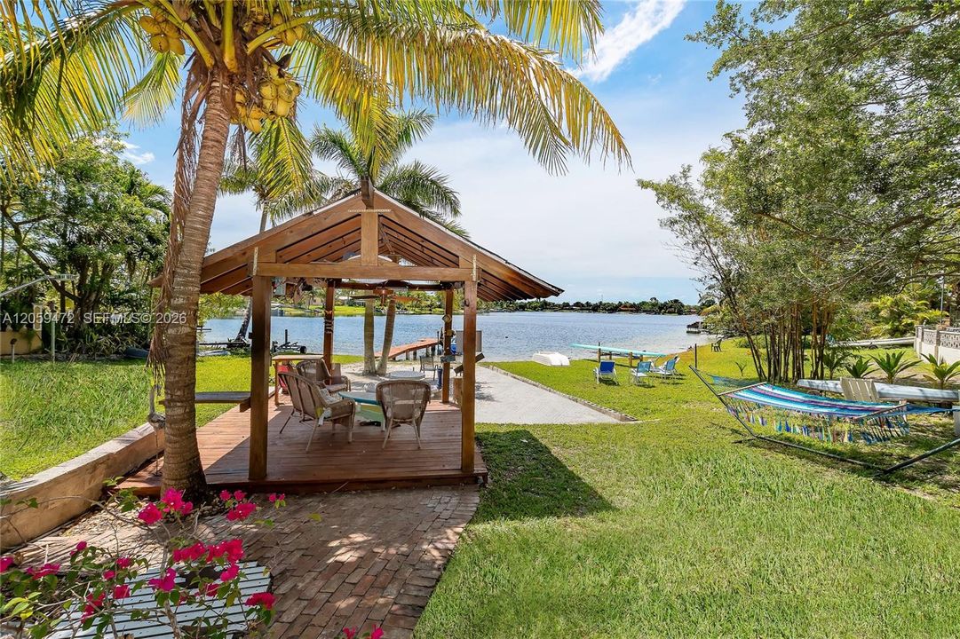 Charming covered gazebo nestled among mature palms and tropical landscaping, connected by a brick path to the waterfront — an idyllic spot to entertain or unwind.
