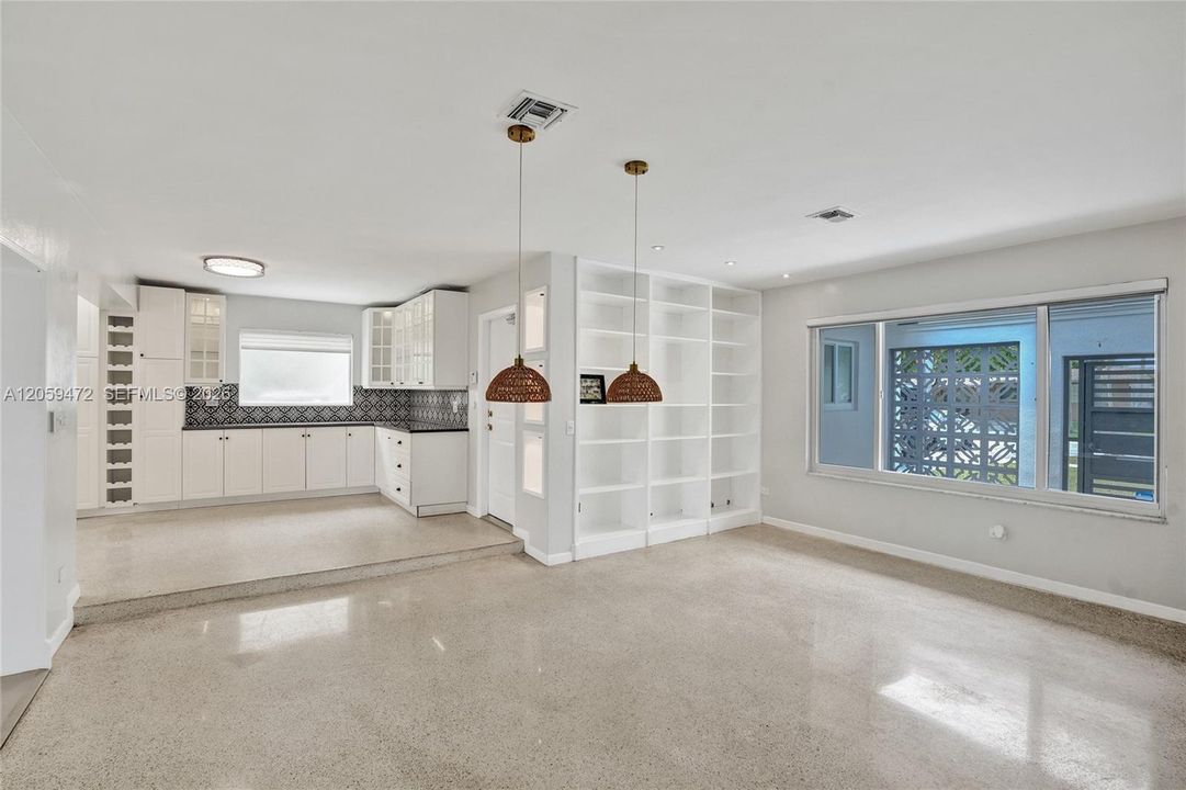 Bright living room with built-in shelving — Featuring polished terrazzo flooring, custom white built-in bookshelves, and a large picture window with decorative breeze-block detail.