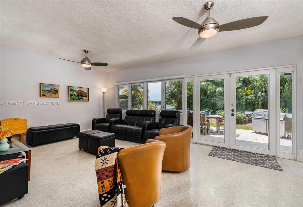 Cozy yet spacious family room featuring a ceiling fan, comfortable seating, and French doors opening to the backyard — ideal for indoor-outdoor living.  FYI - Some paint colors have changed since the last pictures.  Furniture, some lighting fixtures  & personal items not included in the rental