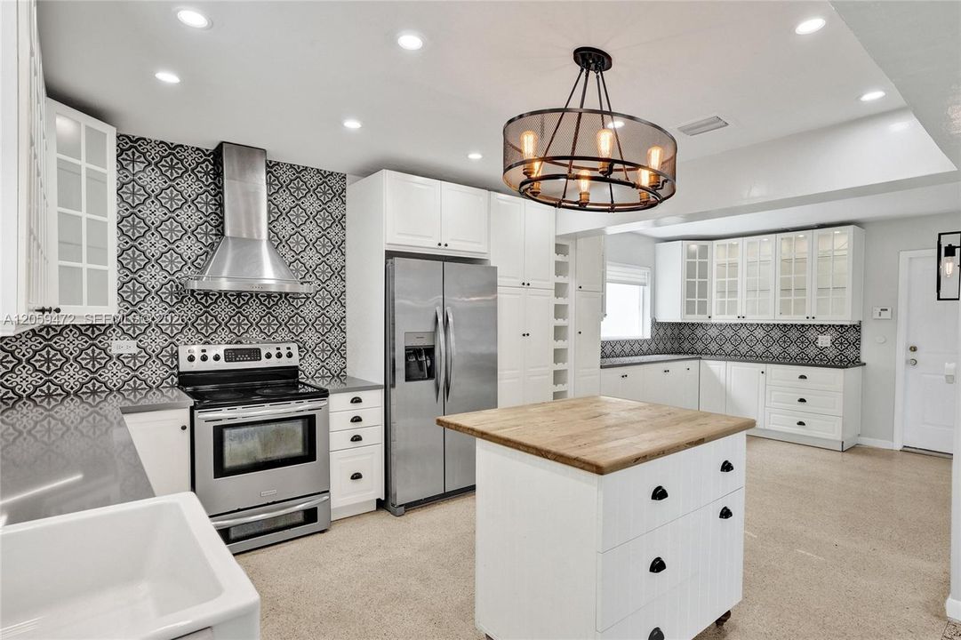 Another angle capturing the kitchen's range and refrigerator wall alongside the full run of cabinetry, with tray ceiling detail and the door leading to your 3-car garage visible in the background — emphasizing the room's generous size and abundant storage.