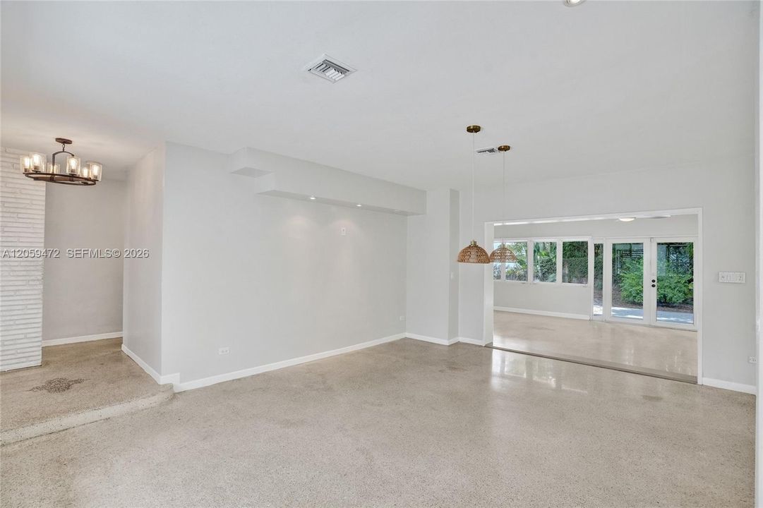 Expansive open-concept living area — Polished terrazzo flooring flows throughout this bright, multi-purpose space featuring custom built-in shelving, woven pendant lighting, and clear sightlines into the updated kitchen and adjacent family room. Impact windows and doors lead out to the backyard, filling the space with natural light. A flexible layout perfect for everyday living and entertaining alike.