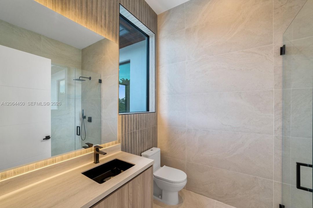 Bathroom featuring large-format stone-finish wall tiles, wood-finish vanity cabinetry, a rectangular vessel sink with matte black hardware, and an expansive frameless glass shower enclosure