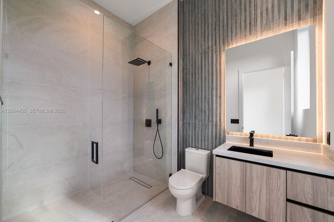 Walk-in shower with a glass enclosure and rain-style showerhead, floating vanity with wood-finish cabinetry, countertop vessel sink, matte black hardware, and textured accent wall