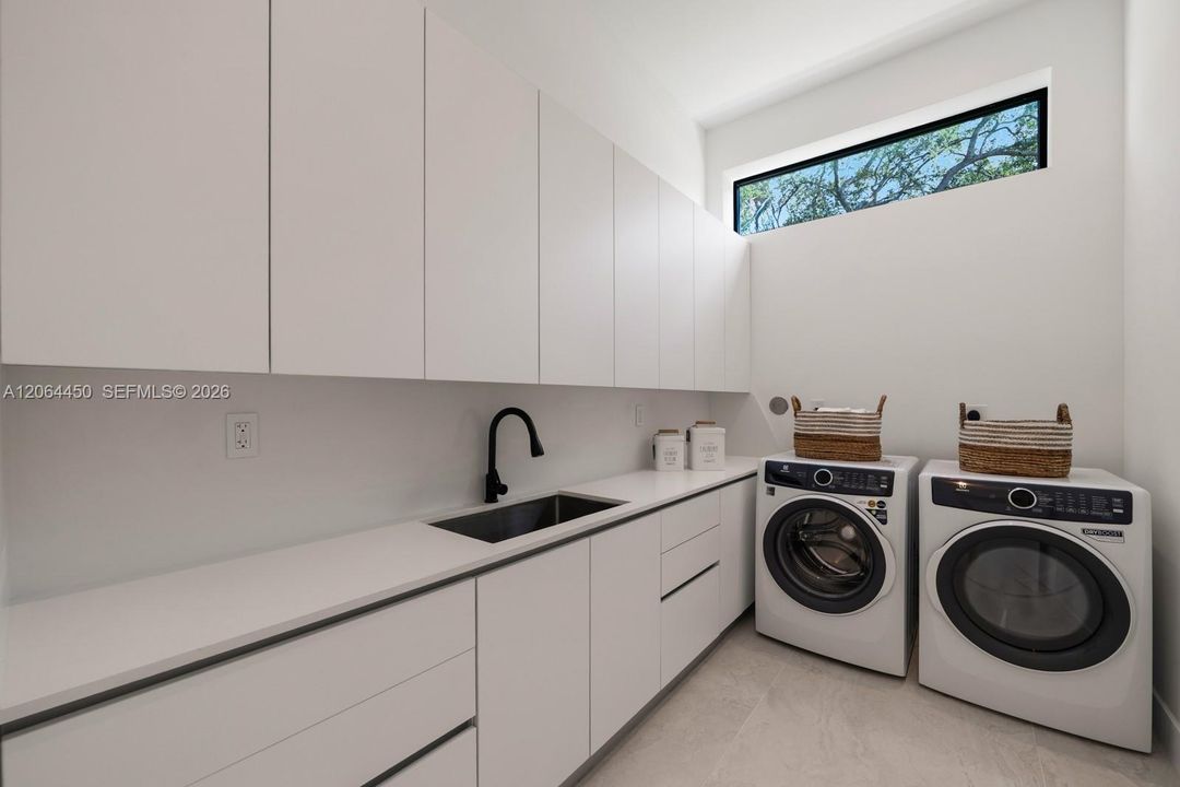 Minimalist utility room featuring floor-to-ceiling white cabinetry, a composite countertop with an integrated basin, a matte black gooseneck faucet, and a clerestory window