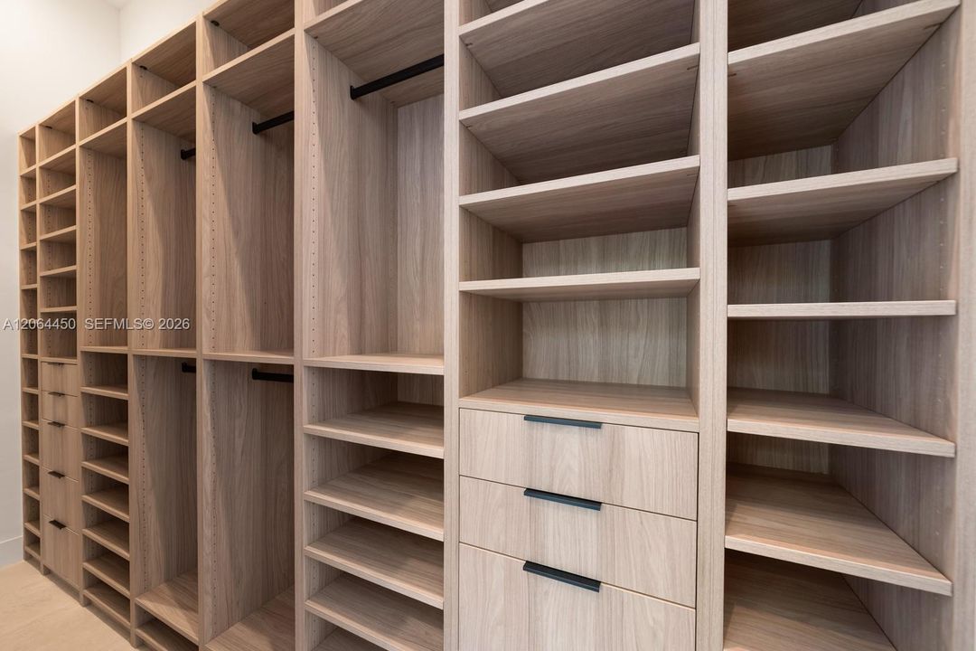 Custom walk-in closet system featuring wood-finish cabinetry, extensive adjustable shelving, integrated hanging rods, and drawers with matte black hardware