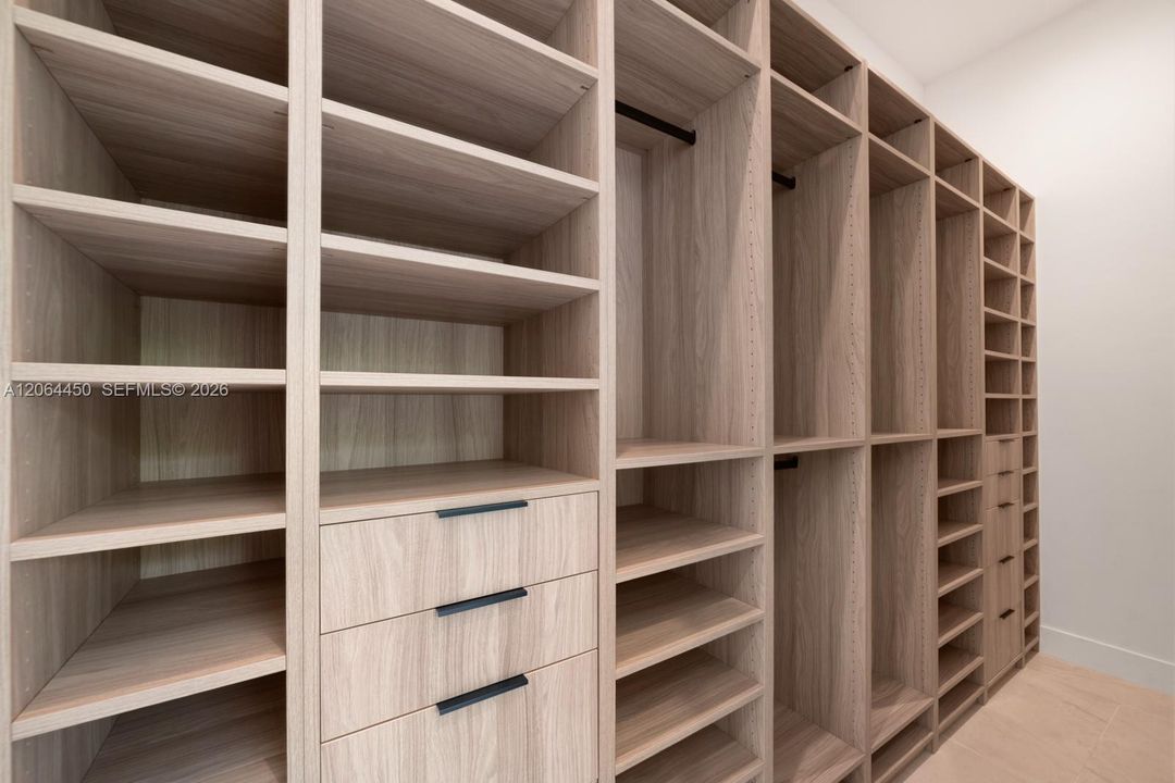 Custom wood-finish shelving unit featuring integrated drawer banks, adjustable open storage cubbies, vertical garment hanging rods, and matte black hardware