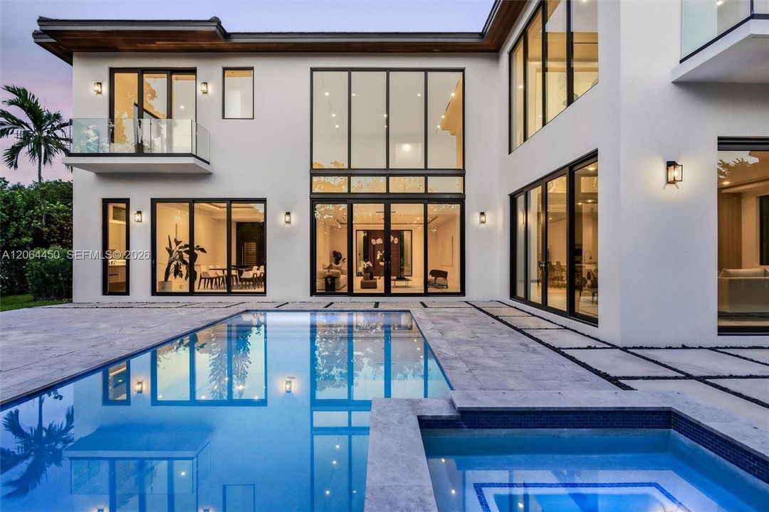Modern exterior featuring floor-to-ceiling glass windows, a swimming pool with a built-in spa, stone paver decking, and a glass-railed balcony