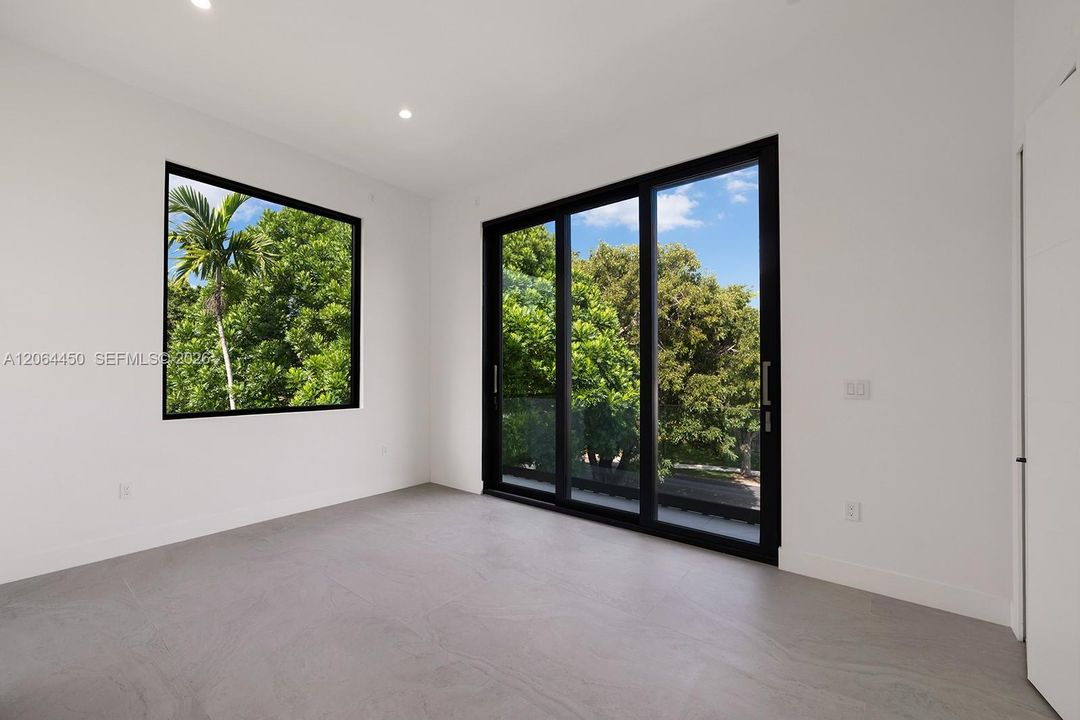 Interior space featuring large-format grey tile flooring, black-framed picture windows, black-framed sliding glass doors, and recessed ceiling lighting