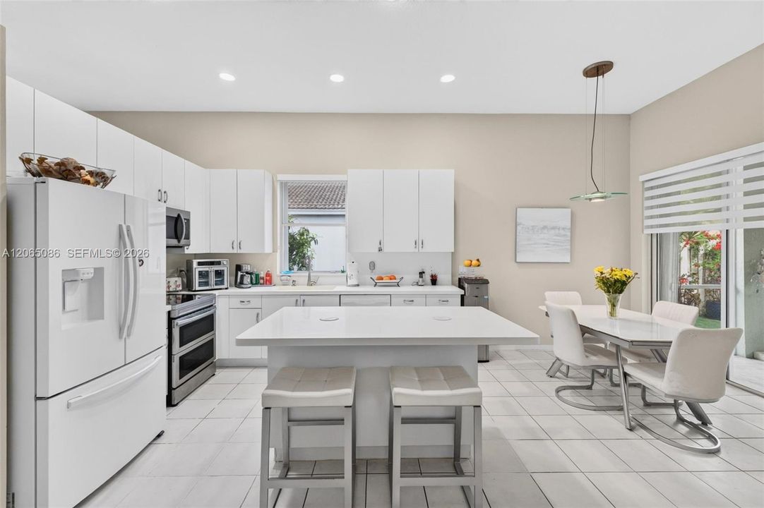 White, bright, open concept kitchen with solid surface counters and roller shades - views looking out to the giant screened, roofed and tiled patio