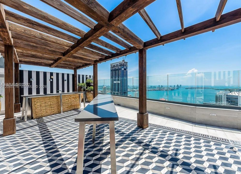 Rooftop terrace featuring a wood pergola, built-in bar, glass panel railing, and geometric patterned tile flooring