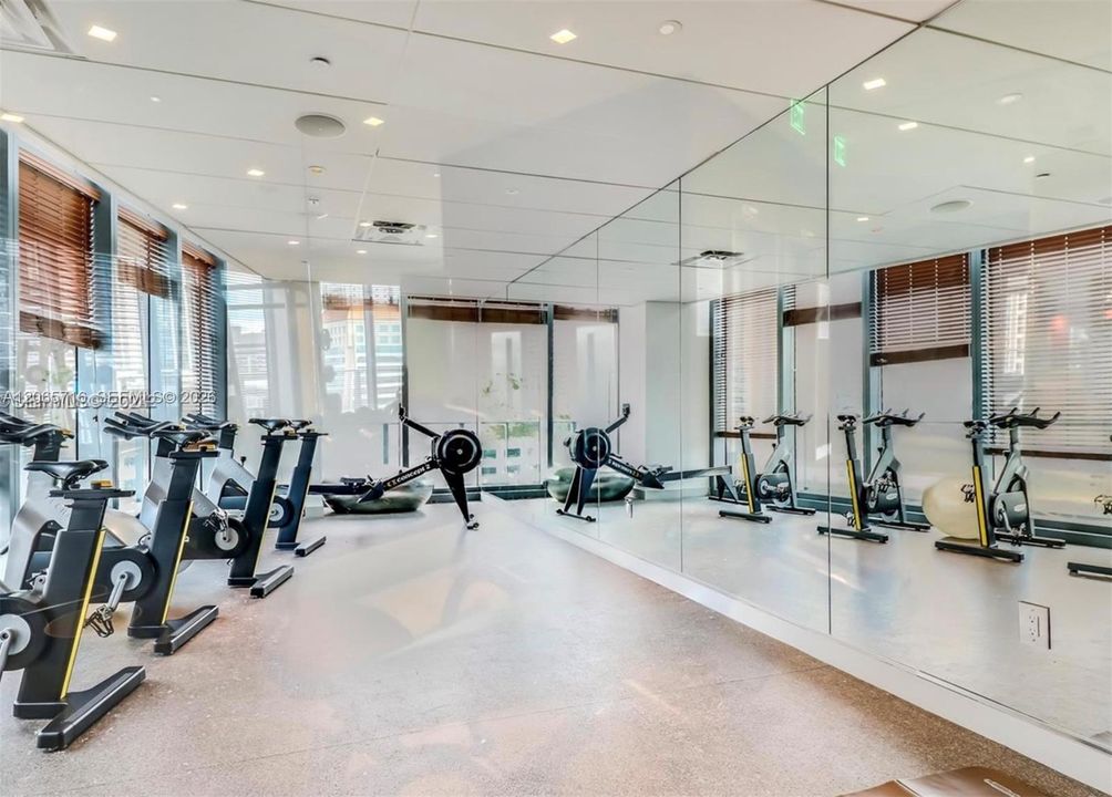 Fitness center featuring floor-to-ceiling mirrored walls, recessed ceiling lighting, and large windows with horizontal blinds