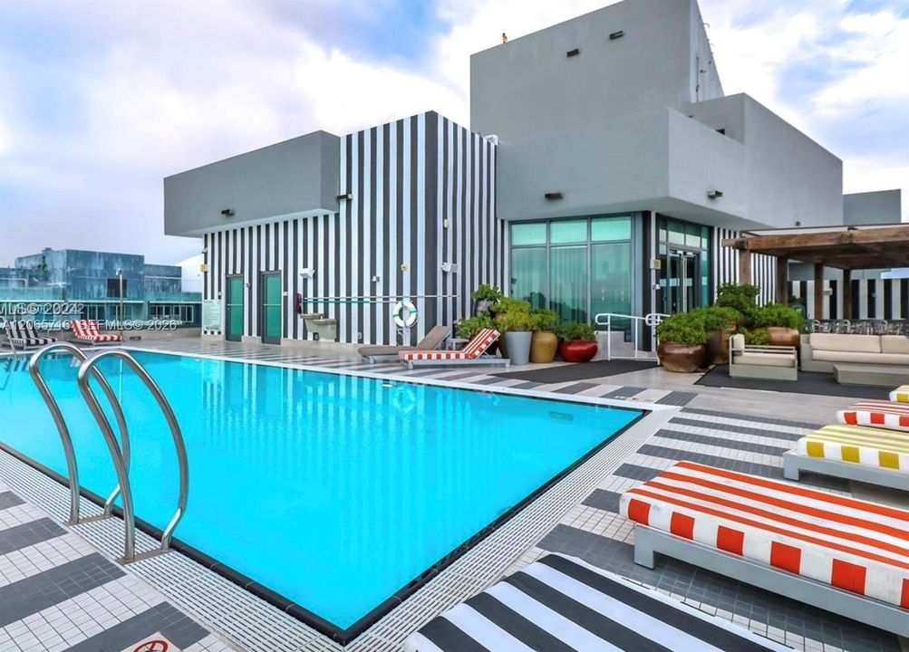 Rooftop swimming pool with stainless steel ladder, tiled pool deck, and integrated wood-frame pergola