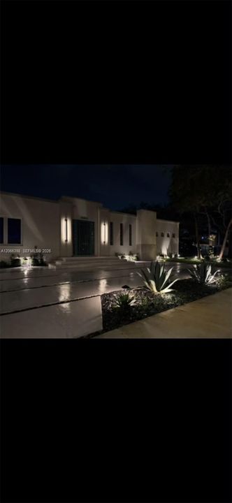 Contemporary exterior featuring smooth stucco finish, structured landscape beds, linear concrete driveway, and vertical wall-mounted lighting