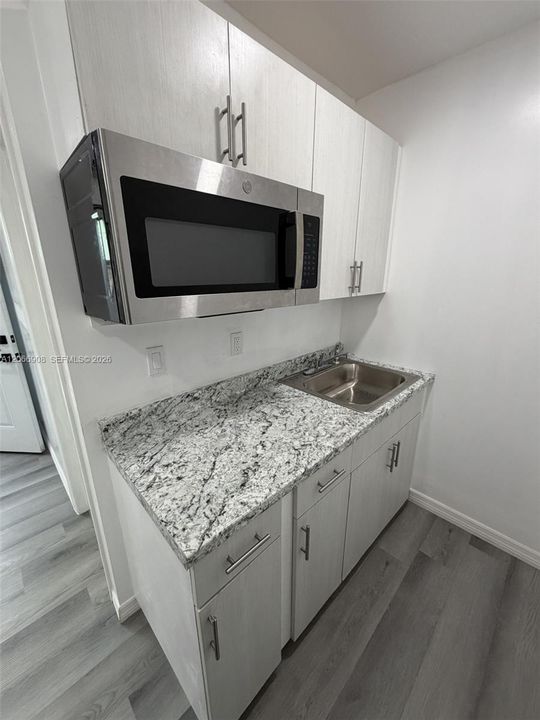 Kitchenette with granite counter, cabinetry, sink, and microwave