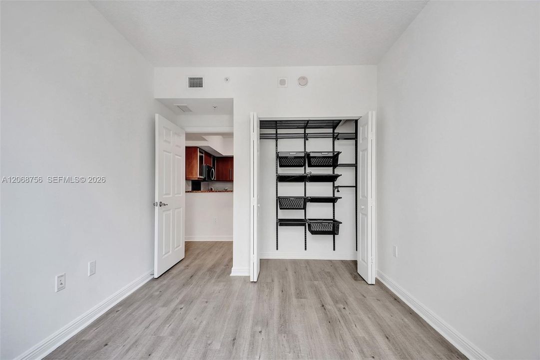 second bedroom, Room featuring wood-finish flooring, white walls, and a closet with installed black metal shelving and basket organizers