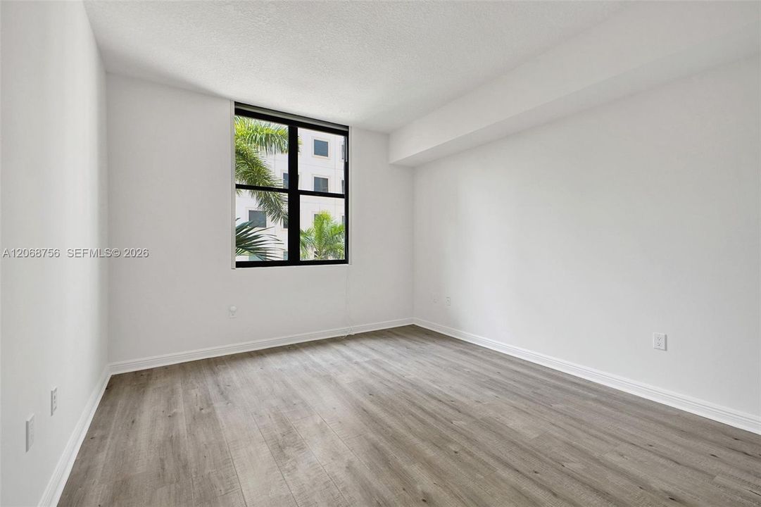 third bedroom, Neutral-toned wood-finish flooring, white walls, and a black-framed window