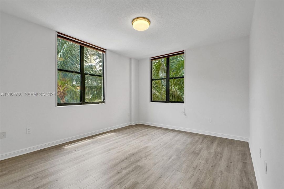 Master bedroom, Interior space featuring wood-finish flooring, two black-framed windows, and a flush-mount ceiling light fixture